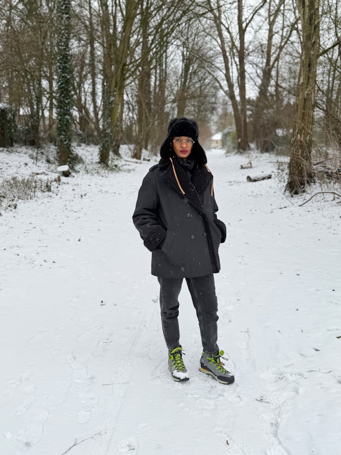 Individual standing on a snowy path in winter attire surrounded by trees.